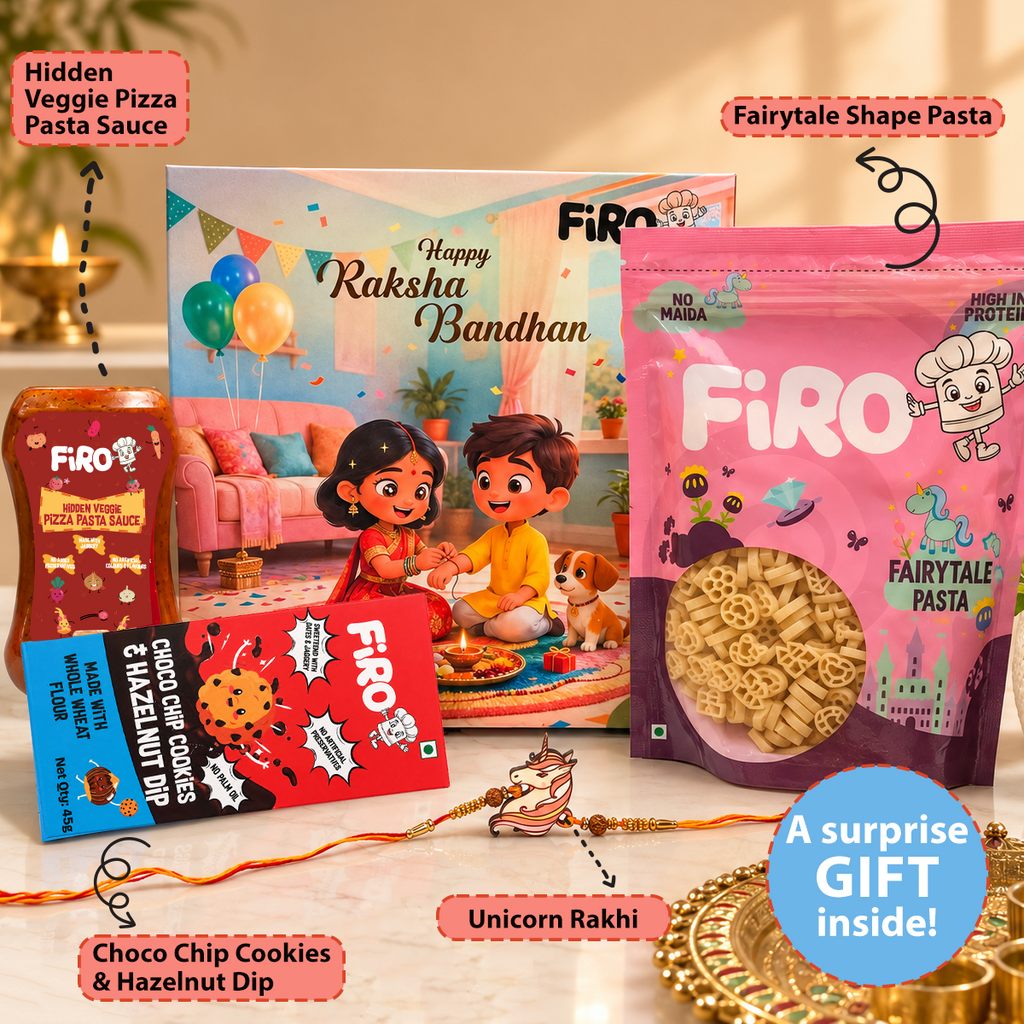 A festive gift set for Raksha Bandhan from Firo, featuring a pink bag of Fairytale Pasta, a bottle of Hidden Veggie Pizza Pasta Sauce, a box of Happy Raksha Bandhan, a pack of Choco Chip Cookies & Hazelnut Dip, and a unicorn-themed Rakhi on a decorated table with text callouts.